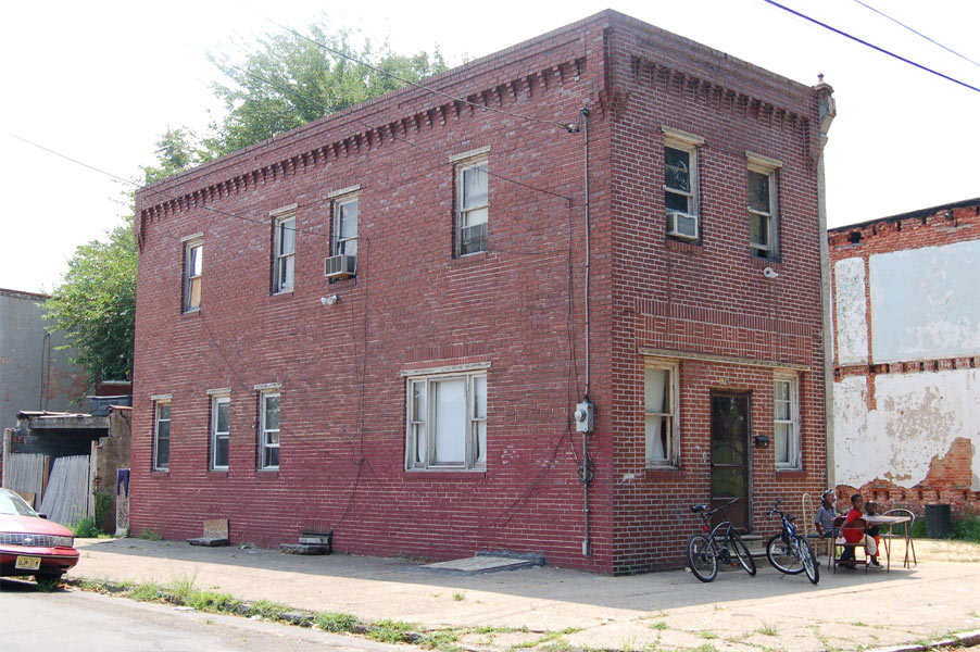 Two-story red brick corner building at 1176 Mount Vernon Street with people seated at a table out front.