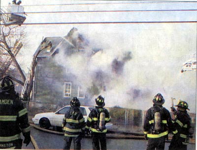 Firefighters in turnout gear watching smoke pour from a burning frame house at 88 Dudley Street